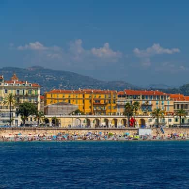A seafront of pastel buildings above a pebble beach, seen from a boat