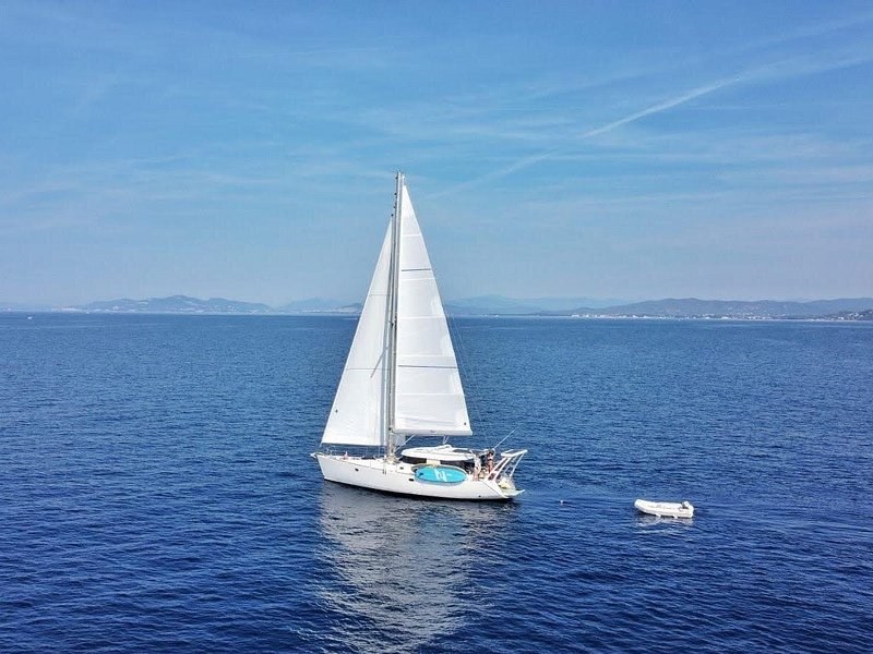 A sailing yacht on open blue water, the coast faint behind