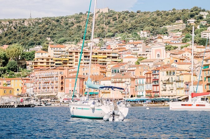 Yachts moored in a small harbour below a hillside of pastel houses